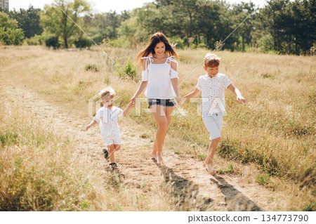 Mother and her two sons enjoy a sunny outdoor walk through a field together. 134773790