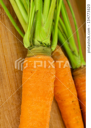 red carrots with green tails lie on the table on a wooden background red carrots with green tails lie on the table on a wooden background 134773820