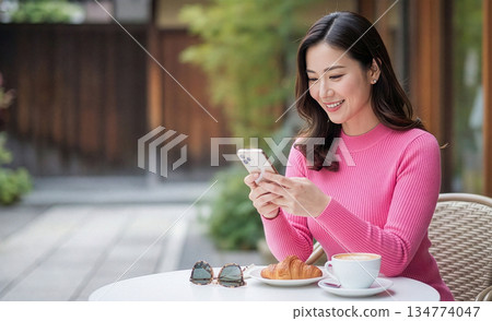 一位女士在露天咖啡館裡面微笑地使用智慧型手機。 134774047