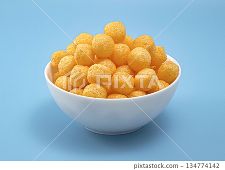 Crunchy cheese corn puff balls snack in white bowl on blue background, full depth of field, copy space Crunchy cheese corn puff balls snack in white bowl on blue background, full depth of field, copy space 134774142