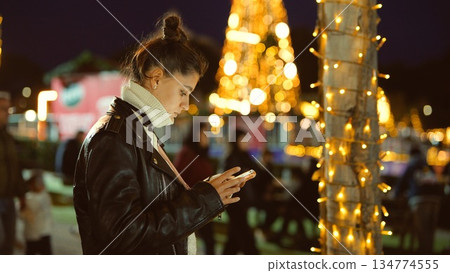Woman wearing leather jacket browsing on her mobile phone at night 134774555