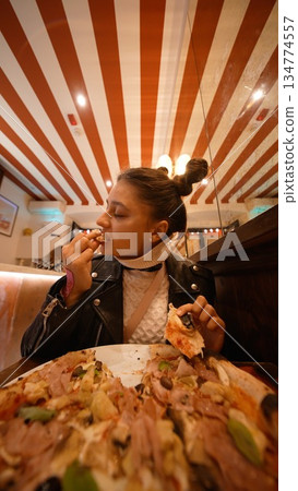 Joyful woman pulls gooey mozzarella pizza slice with delight Joyful woman pulls gooey mozzarella pizza slice with delight 134774557