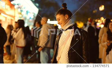 Female individual engaged with mobile amidst bustling market ambiance Female individual engaged with mobile amidst bustling market ambiance 134774571