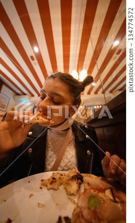 Woman savoring final pizza bite with playful expression Woman savoring final pizza bite with playful expression 134774572