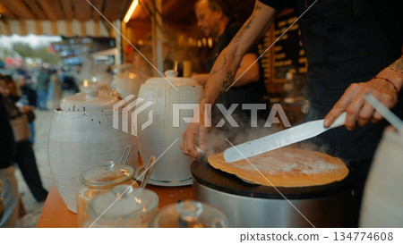 Vendor spreading batter on sizzling griddle with bustling crowd behind Vendor spreading batter on sizzling griddle with bustling crowd behind 134774608