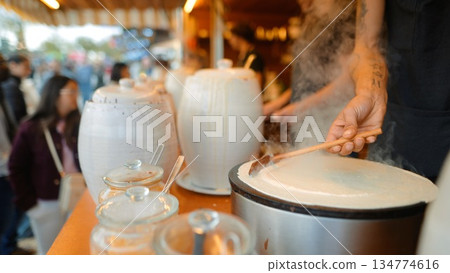 vendor pouring crepe batter while customer watches at stall 134774616