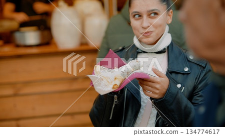 Smiling young woman presents sample at lively market stall Smiling young woman presents sample at lively market stall 134774617