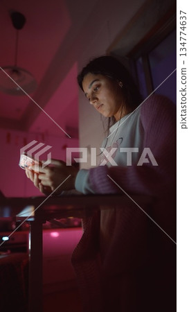 Female individual responds to texts while gazing outside at night 134774637