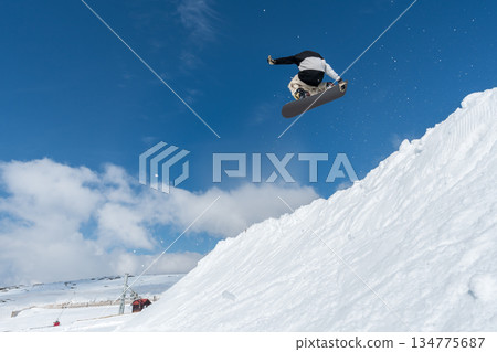 Snowboarder jumping against blue sky Snowboarder jumping against blue sky 134775687