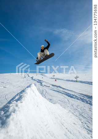Snowboarder jumping against blue sky 134775698