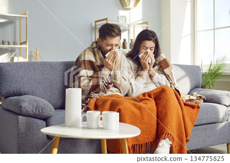 Young couple blowing their nose in tissue at home Young couple blowing their nose in tissue at home 134775825