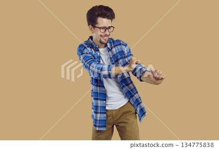 Funny nerdy student in plaid shirt and glasses dancing isolated on beige background Funny nerdy student in plaid shirt and glasses dancing isolated on beige background 134775838