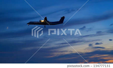 A passenger plane flying through the evening sky under a crescent moon 134777131