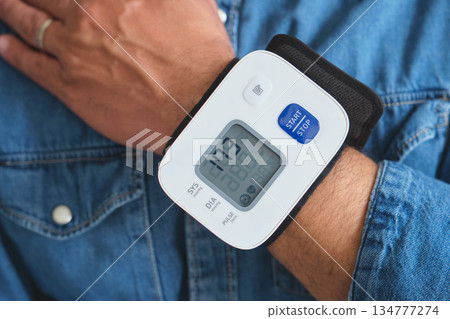 Man checking his blood pressure with a digital wrist monitor Man checking his blood pressure with a digital wrist monitor 134777274