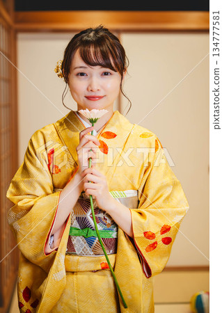 一位身著和服的美麗年輕女子手捧鮮花，站在日式房間裡。 134777581