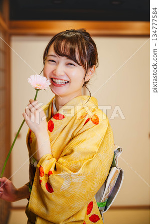 一位身著和服的美麗年輕女子手捧鮮花，站在日式房間裡。 134777584