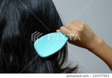 Back view of a woman arranging her glossy black hair with a hairbrush Back view of a woman arranging her glossy black hair with a hairbrush 134777953