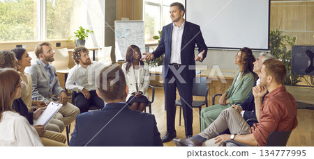 Cowokers listening to their male colleague sitting in a circle in a meeting room. Cowokers listening to their male colleague sitting in a circle in a meeting room. 134777995