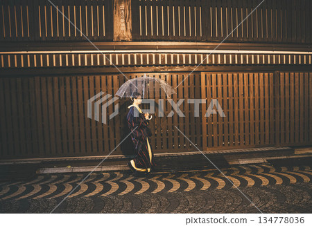雨夜裡，一位穿著和服的年輕女子撐著傘站在城市街頭。 134778036