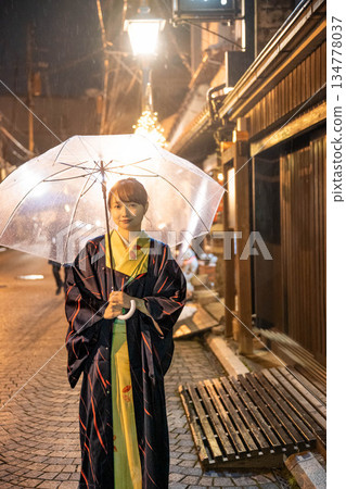 A young woman in a kimono standing with an umbrella in the city at night on a rainy day A young woman in a kimono standing with an umbrella in the city at night on a rainy day 134778037
