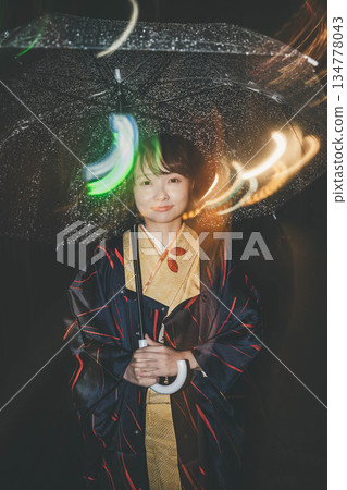 雨夜裡，一位穿著和服的年輕女子撐著傘站在城市街頭。 134778043