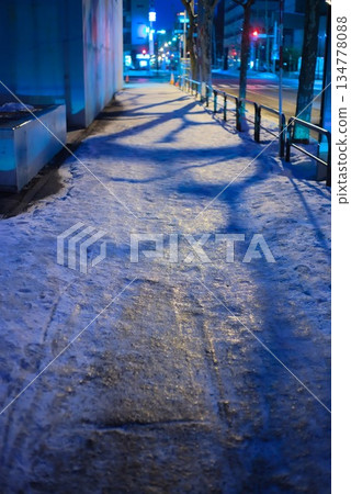 夜幕下的城市人行道，路燈的光芒映照在冰雪覆蓋的路面上。 134778088