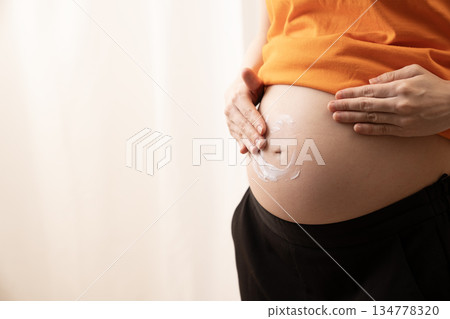 Woman applying cream to her 8-month pregnant belly Woman applying cream to her 8-month pregnant belly 134778320