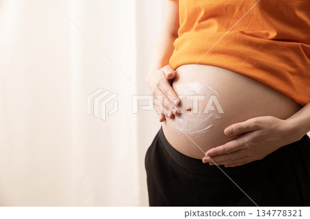 一名婦女在懷孕 8 個月的腹部塗抹乳霜 一名婦女在懷孕 8 個月的腹部塗抹乳霜 134778321