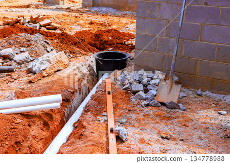 Workers are installing drainage system at construction site with exposed soil, tools nearby. 134778988