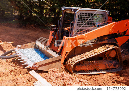 Heavy excavator is working on construction site moving gravel with loader in residential location. 134778992