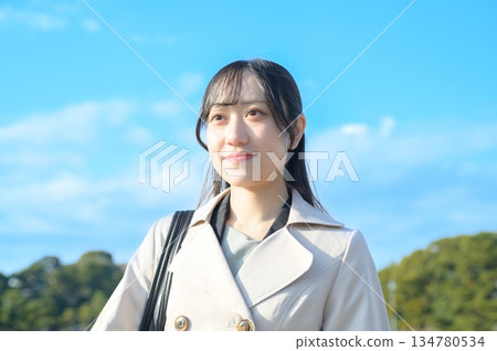 A woman in a coat smiling against the blue sky A woman in a coat smiling against the blue sky 134780534