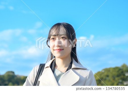 A woman in a coat smiling against the blue sky A woman in a coat smiling against the blue sky 134780535