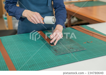Woman tanner processes the edges of a leather belt in a workshop.  134780640