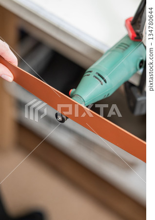 Leatherworker grinding the edge of a strip of leather for a belt in the workshop. Leatherworker grinding the edge of a strip of leather for a belt in the workshop. 134780644