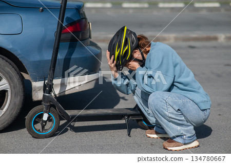 A distressed woman examines the damage after a collision between an electric scooter and a car. A distressed woman examines the damage after a collision between an electric scooter and a car. 134780667