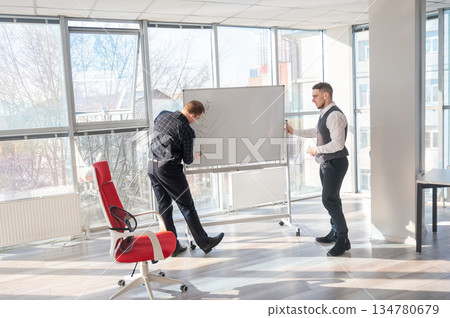Two Caucasian men discussing work at a white board. Two Caucasian men discussing work at a white board. 134780679