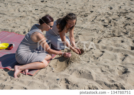 Two Caucasian women relax on the beach and build sand castles. Two Caucasian women relax on the beach and build sand castles. 134780751