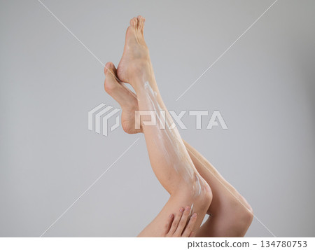 Woman applying moisturizer to her legs. White background. Woman applying moisturizer to her legs. White background. 134780753
