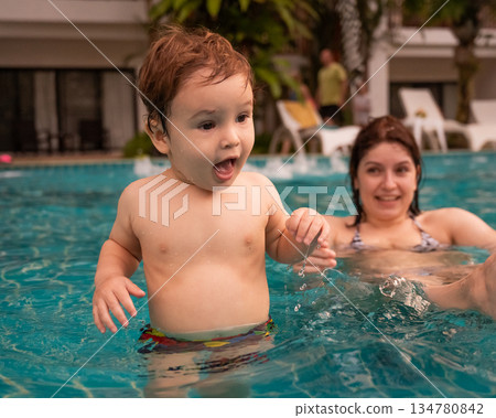 Caucasian woman holds her son while swimming in a pool on vacation. Mom teaches little boy to swim. Caucasian woman holds her son while swimming in a pool on vacation. Mom teaches little boy to swim. 134780842