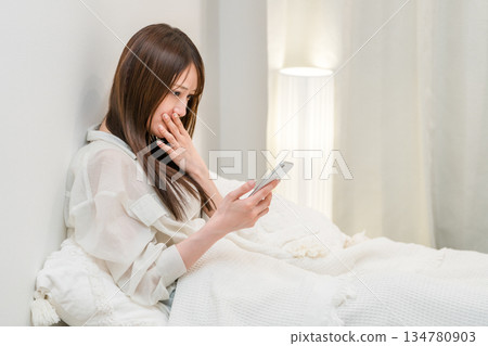 Young Asian woman in bed at night looking at her smartphone Young Asian woman in bed at night looking at her smartphone 134780903