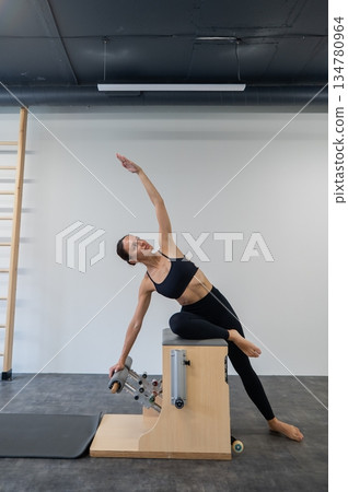 Caucasian woman doing Pilates on classic chair. Caucasian woman doing Pilates on classic chair. 134780964