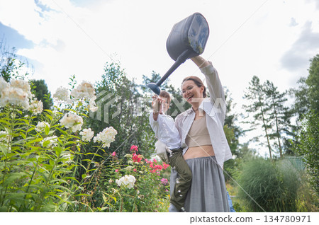 Caucasian woman and her son watering flowers in the garden. Caucasian woman and her son watering flowers in the garden. 134780971