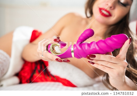 Caucasian woman in santa claus costume and stockings lies on bed with sex toy. Caucasian woman in santa claus costume and stockings lies on bed with sex toy. 134781032