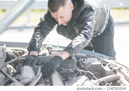A man changes spark plugs in his car.  134781034
