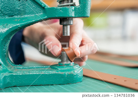 A woman attaches accessories to a leather belt. Leatherworker's workshop.  134781036