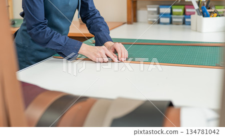 Leatherworker measuring and cutting leather in workshop. Leatherworker measuring and cutting leather in workshop. 134781042