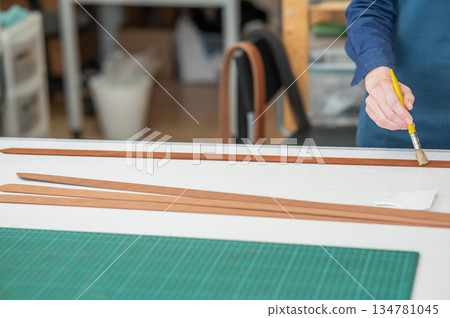 A craftsman uses a brush to cover leather parts. A craftsman uses a brush to cover leather parts. 134781045