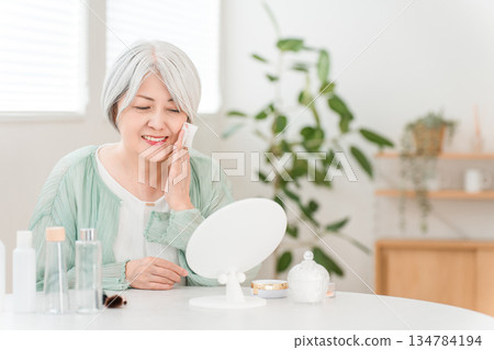 一位頭髮花白的老婦人使用保養品滋潤肌膚 一位頭髮花白的老婦人使用保養品滋潤肌膚 134784194