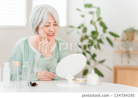 一位頭髮花白的老婦人使用保養品滋潤肌膚 一位頭髮花白的老婦人使用保養品滋潤肌膚 134784195