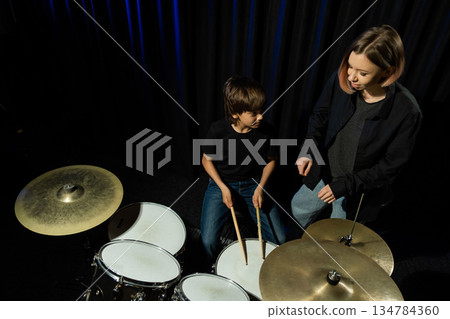 Young caucasian woman teaches a boy to play the drums in the studio on a black background. Music school student 134784360